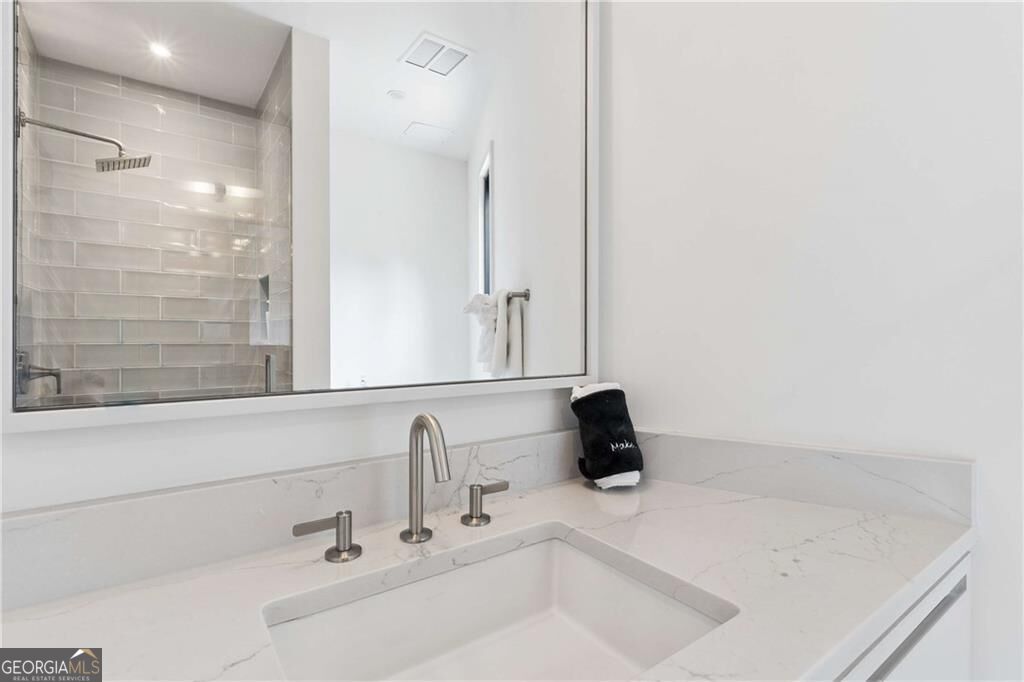 Bathroom vanity with a veined white countertop, rectangular sink, large mirror, and gray subway-tile shower.
