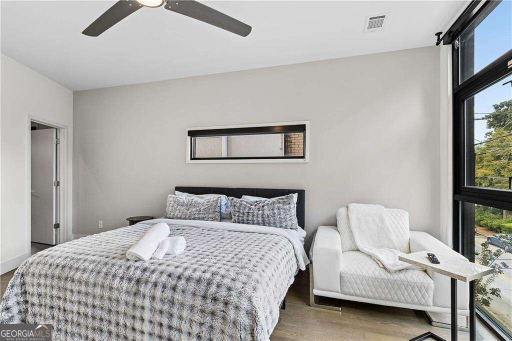 Staged bedroom with a large bed beside a white chair and tall black-framed windows.