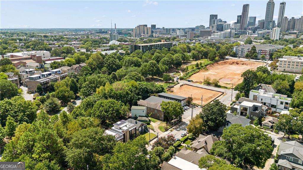 Aerial view of a cleared construction site amid leafy Atlanta neighborhoods, with the downtown skyline beyond.
