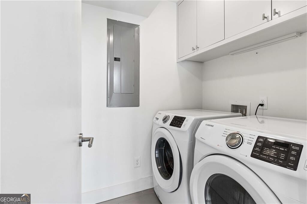 Laundry room with front-loading washer and dryer beneath white cabinets.