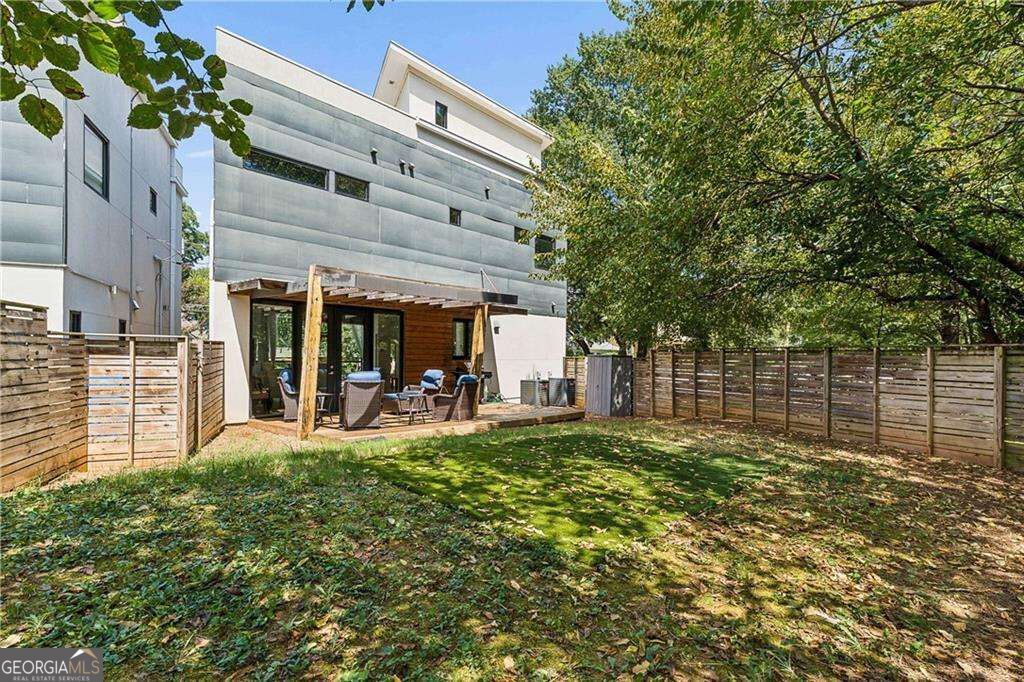 Modern home with a pergola-covered patio opening onto a fenced, tree-shaded backyard.