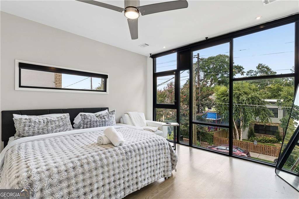 Bedroom with a large bed and floor-to-ceiling windows overlooking trees and nearby homes.