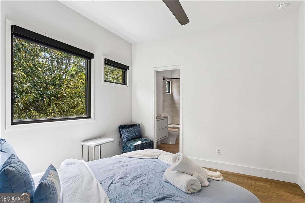 Bedroom with pale blue bedding, a blue chair, and large windows overlooking leafy trees.