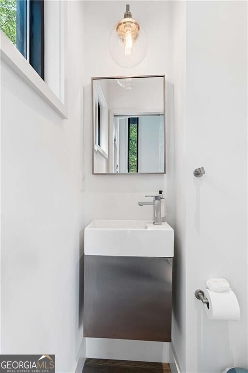 Compact bathroom with a dark floating vanity, rectangular sink, framed mirror, and glass pendant light.