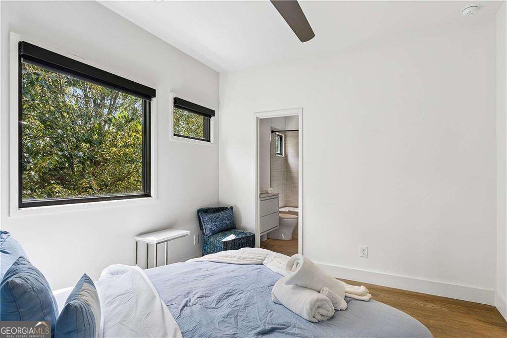 Bedroom with blue bedding, leafy views through large windows, and an en-suite bathroom.