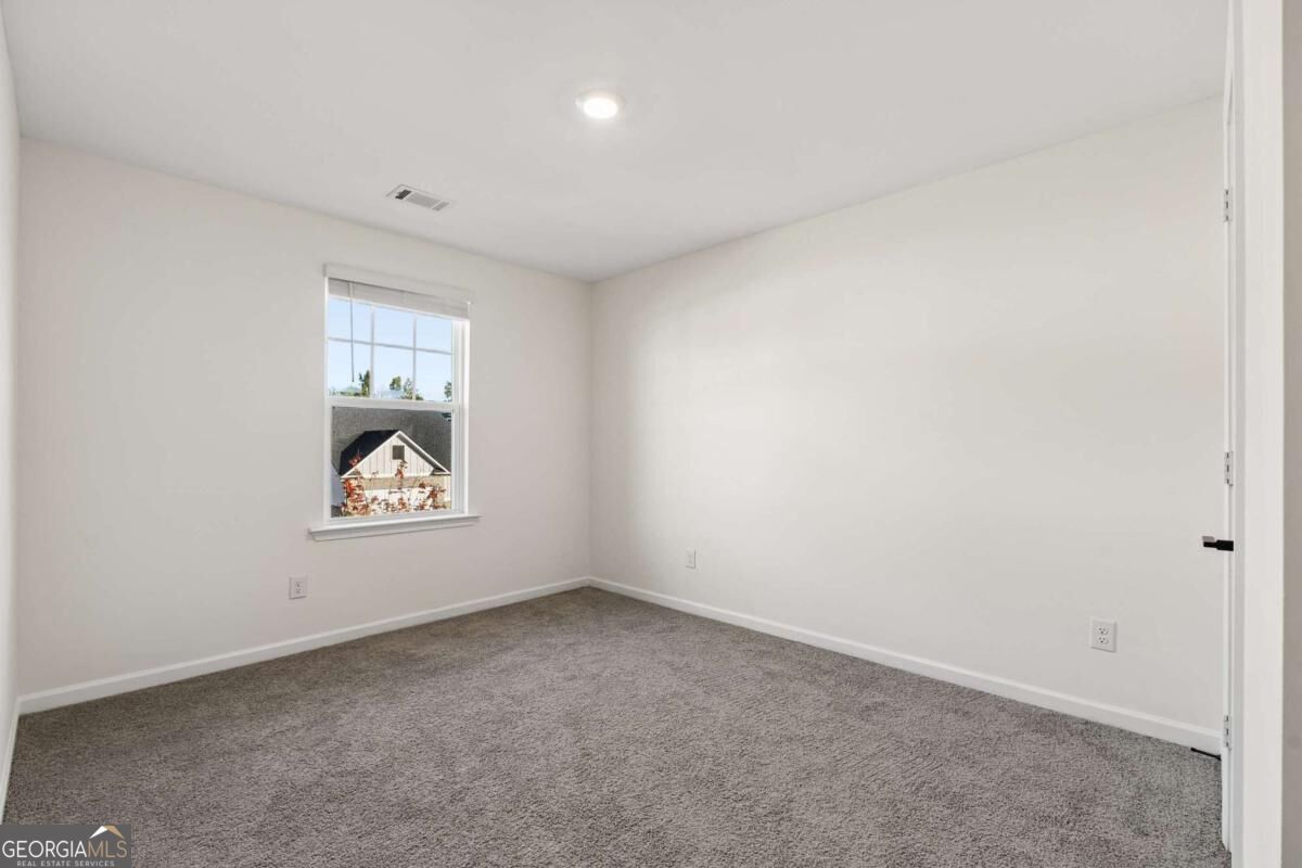 Empty carpeted bedroom with white walls and a window overlooking a neighboring house.