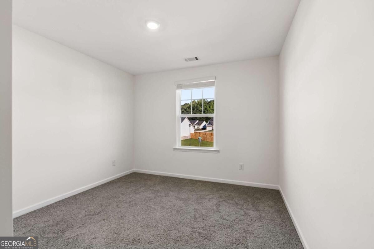 Empty carpeted bedroom with a single window overlooking neighboring homes.