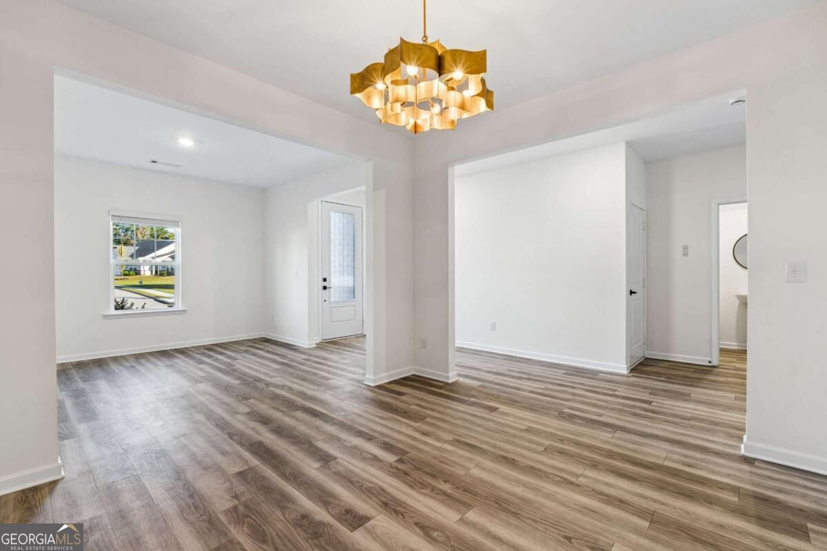 Empty open interior with wood-look floors, a gold chandelier, and the front door.