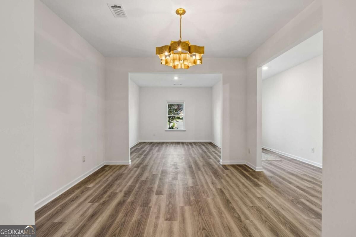 Empty dining room with plank flooring and a gold chandelier.