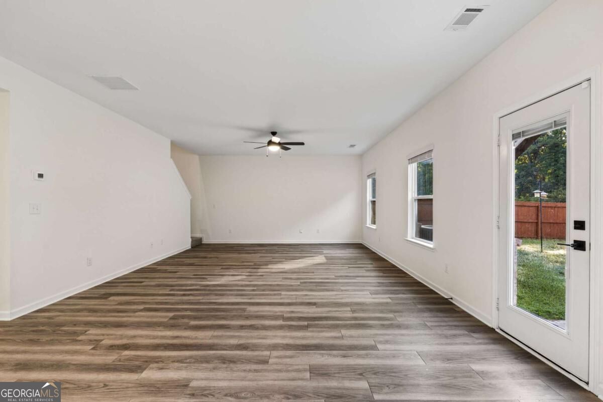 Empty living room with wood-look flooring, ceiling fan, and a glass-paned exterior door.