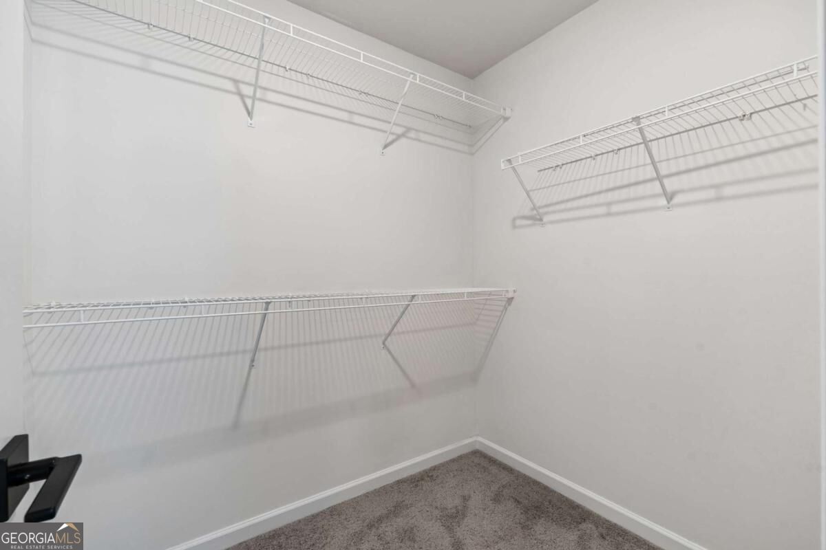 Empty walk-in closet with white wire shelves on three walls and gray carpet.