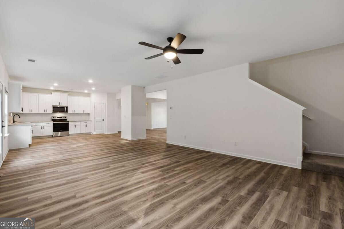 Open kitchen and living area with white cabinets, wood-look flooring, and a staircase.