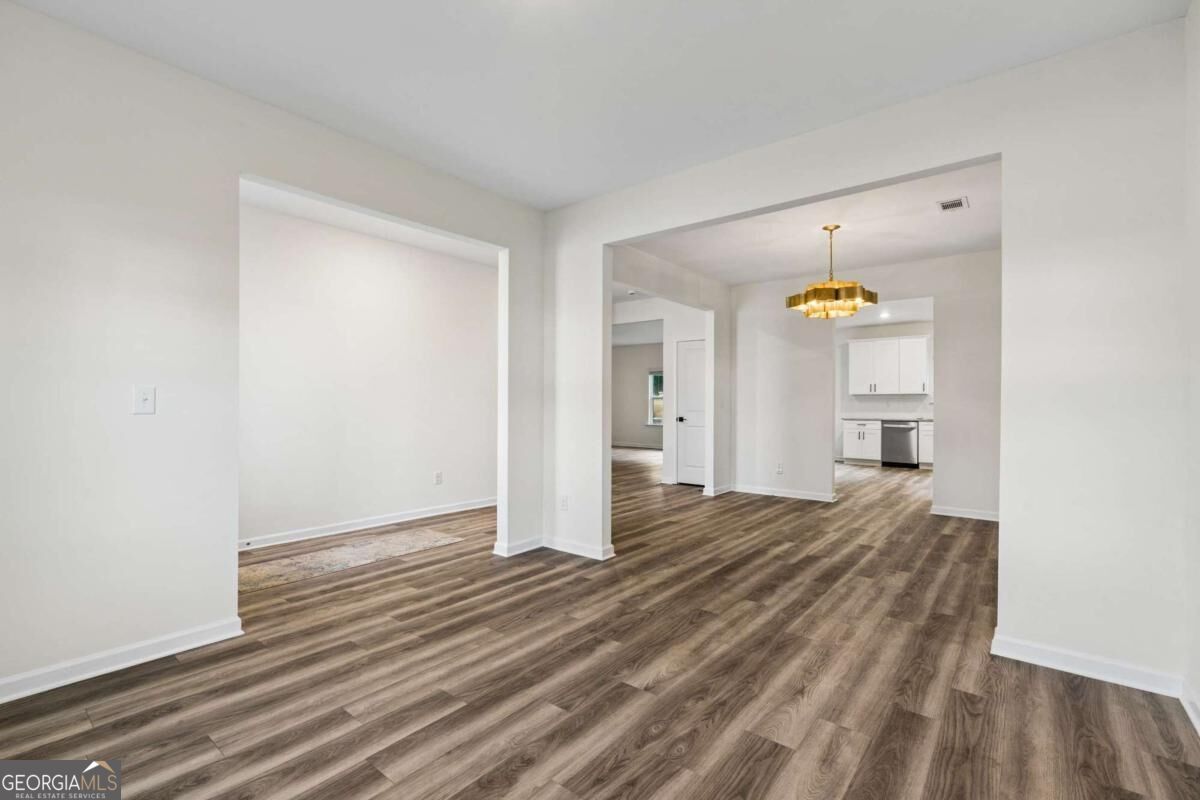 Empty open-plan dining area with wood-look floors, a gold chandelier, and the kitchen beyond.