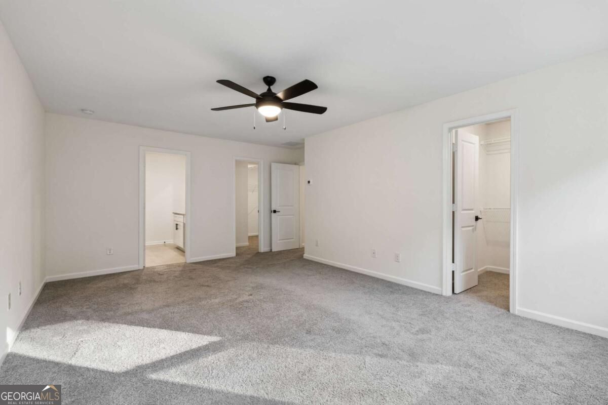 Empty carpeted bedroom with a dark ceiling fan and sunlight across the floor.