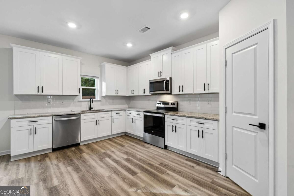Renovated kitchen with white cabinets, stainless steel appliances, and wood-look flooring.