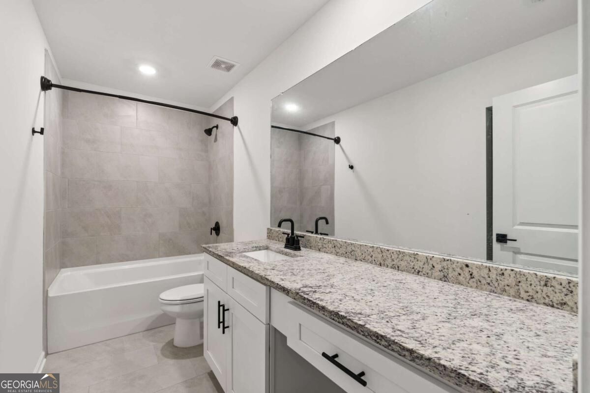 Bathroom with a tiled tub surround and long white vanity topped with speckled granite.