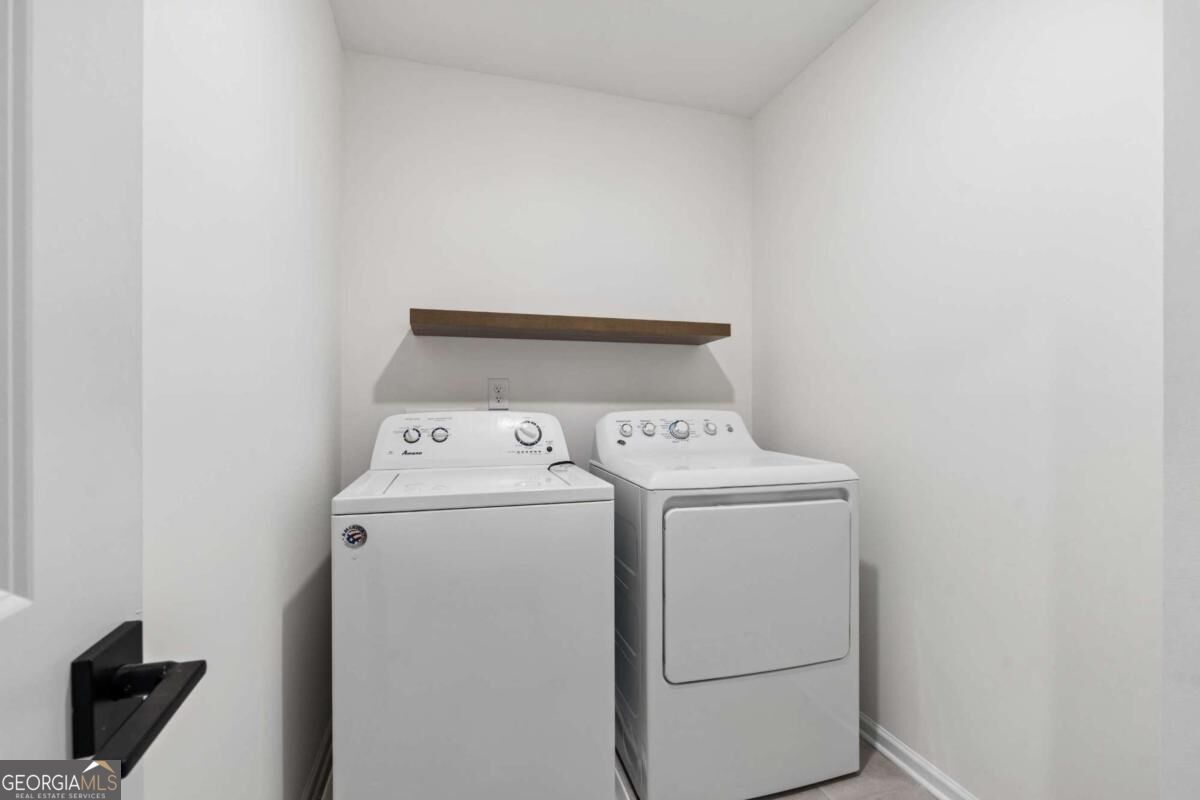 Laundry room with a top-loading washer and front-loading dryer beneath a floating wood shelf.