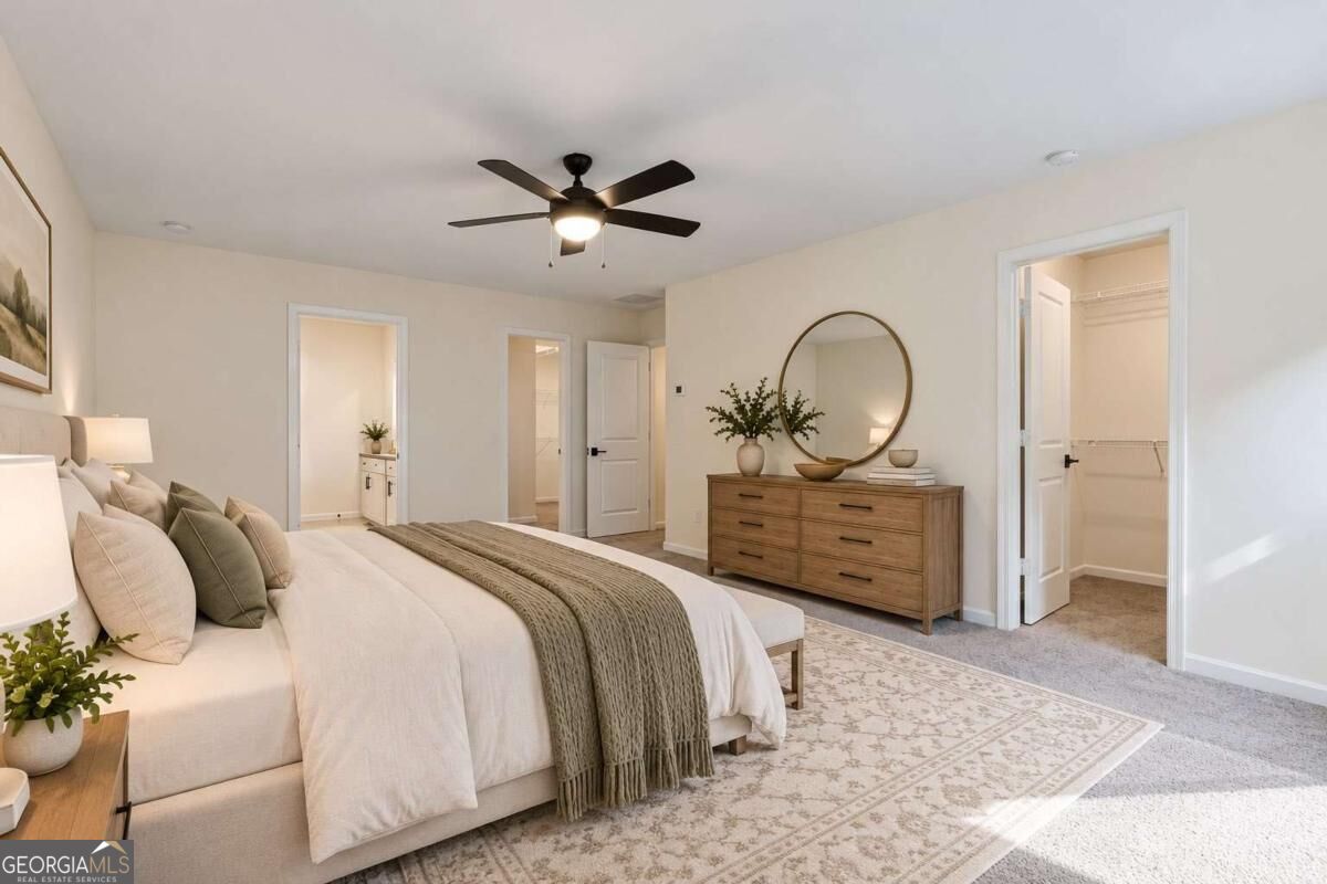 Staged bedroom with a neutral upholstered bed, wooden dresser, round mirror, and walk-in closet.