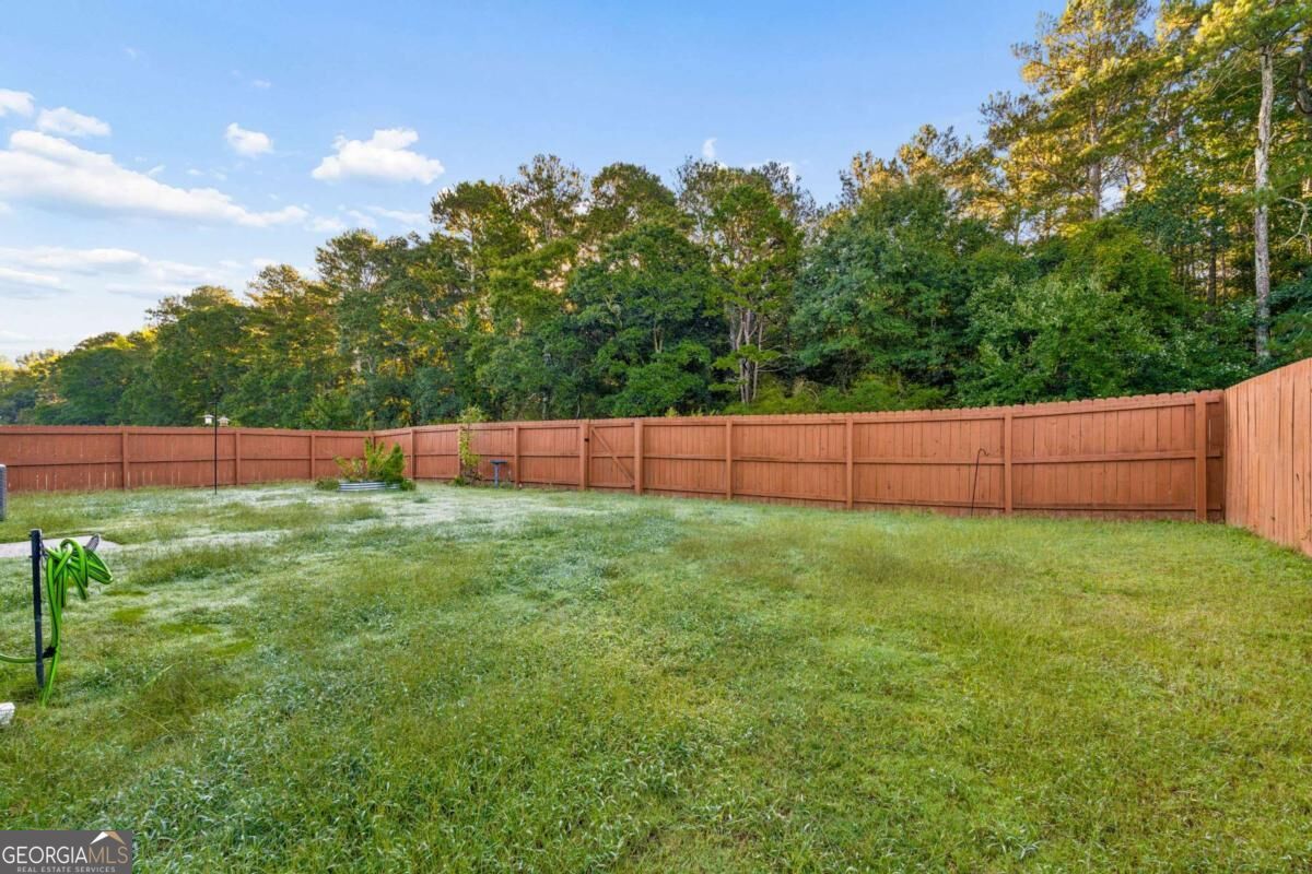 Fenced backyard with a broad lawn, reddish wooden privacy fence, and wooded tree line.