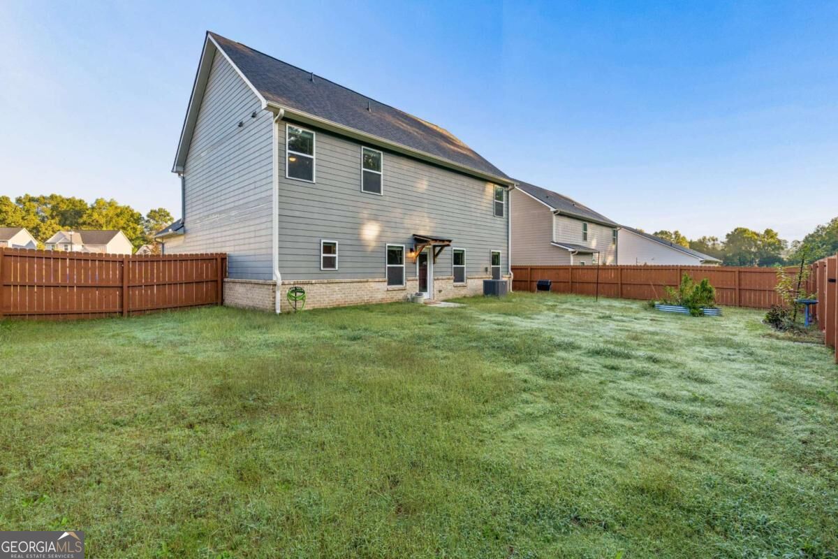 Rear exterior of a two-story gray-sided home with a fenced lawn and covered back door.