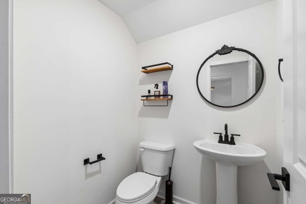 Bathroom with a pedestal sink, toilet, black fixtures, and an oval mirror.