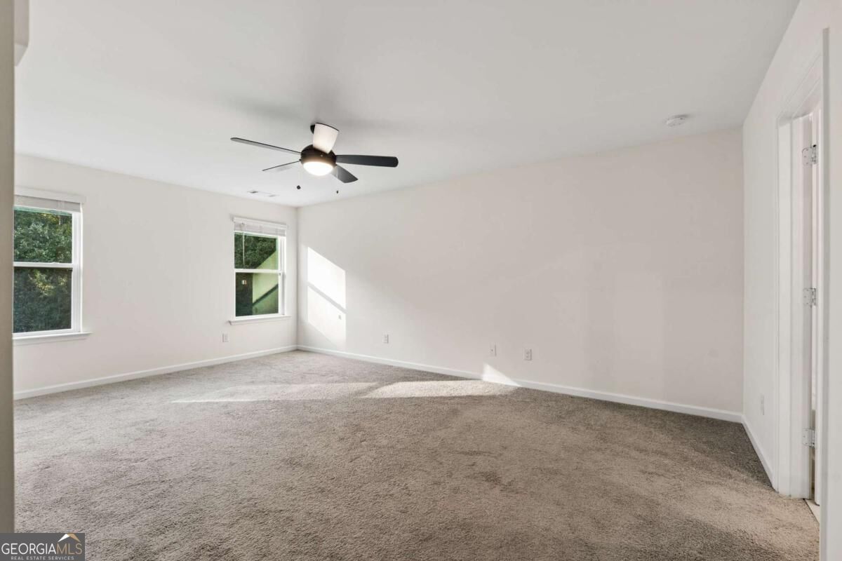 Empty carpeted room with a ceiling fan and two windows.