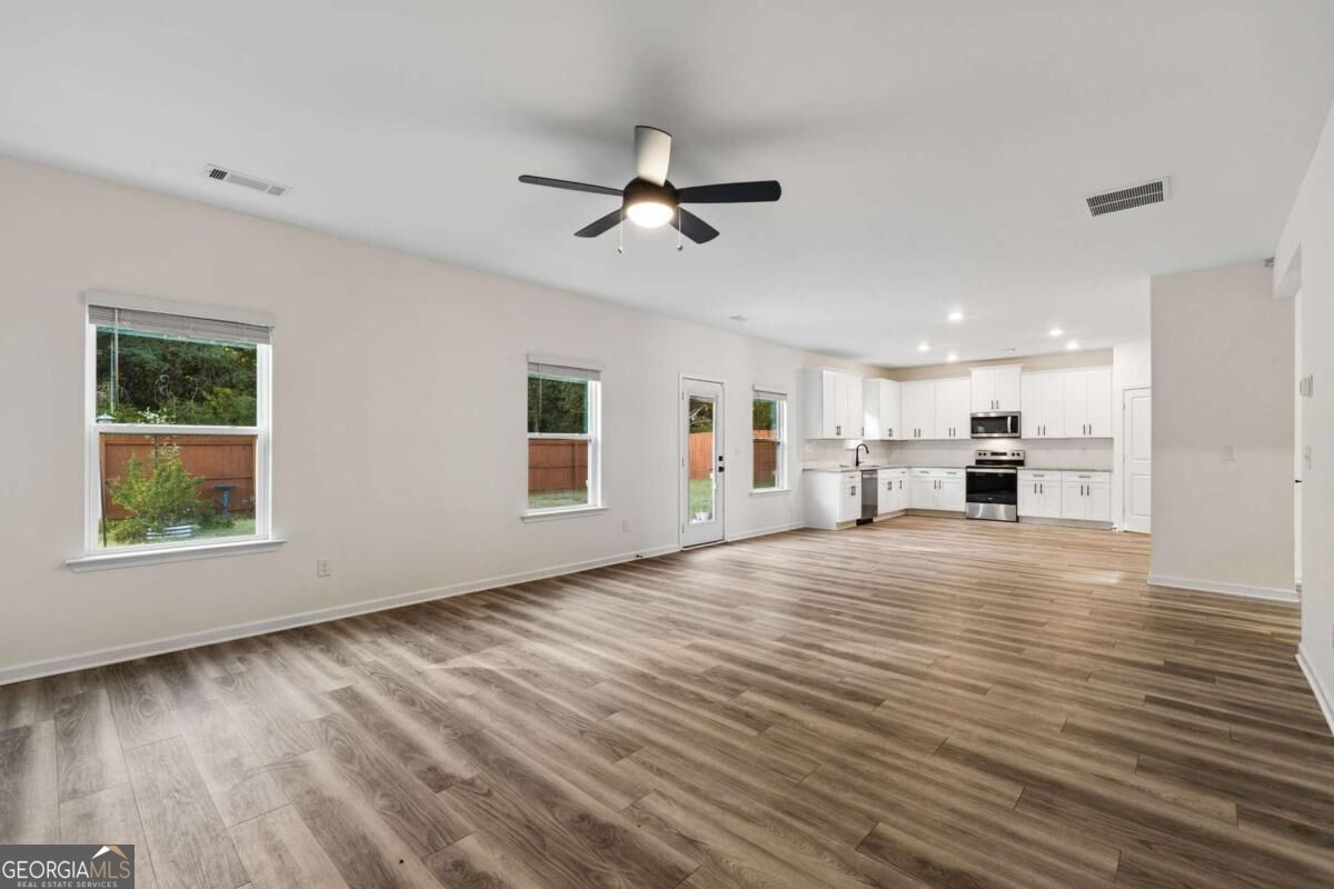 Open-plan living area with wood-look flooring, ceiling fan, and white kitchen.