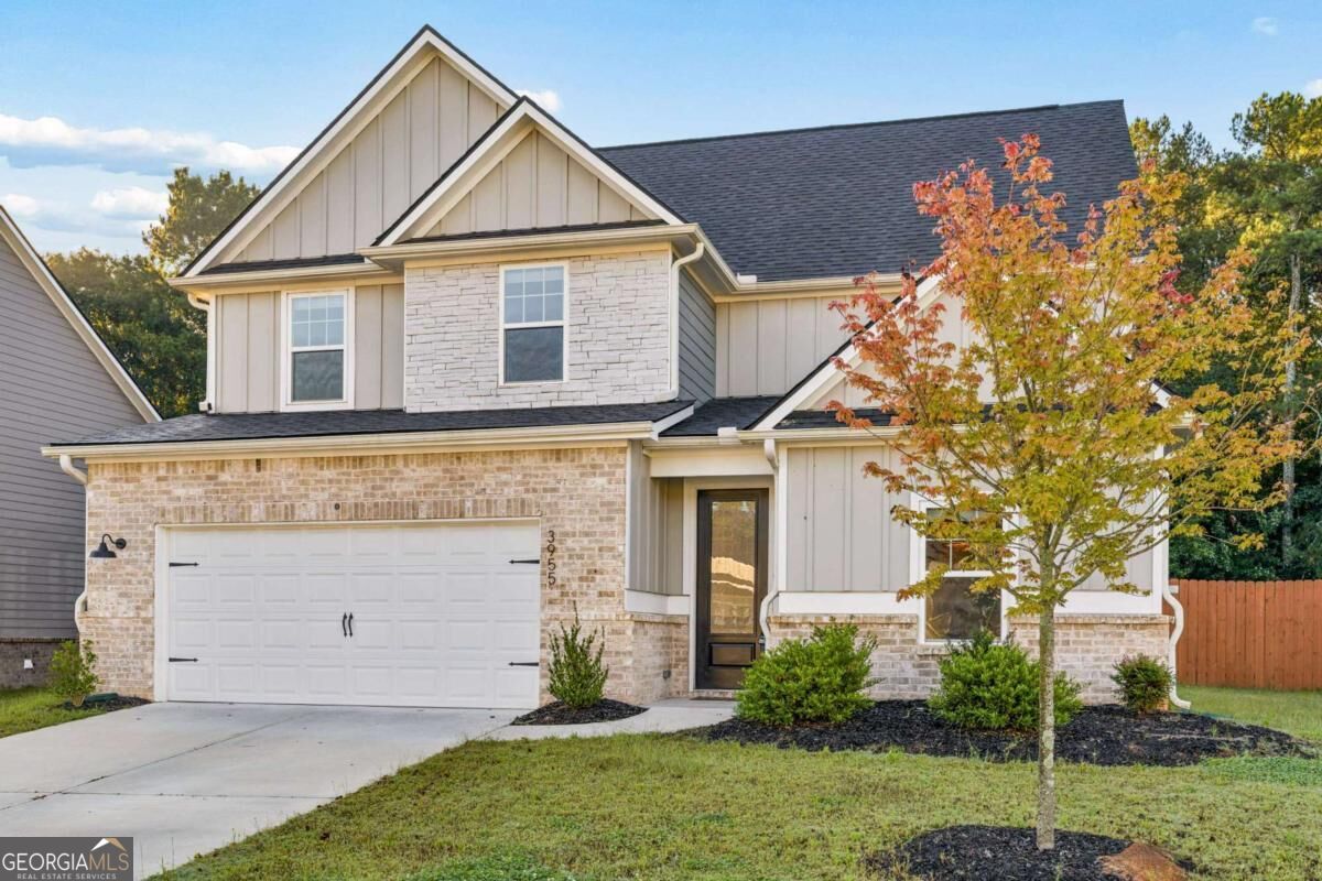 Two-story home with stone veneer, a two-car garage, and an autumn-colored tree in the front yard.