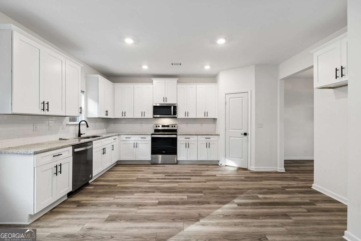 Kitchen with white shaker cabinets, stainless steel appliances, and wood-look plank flooring.