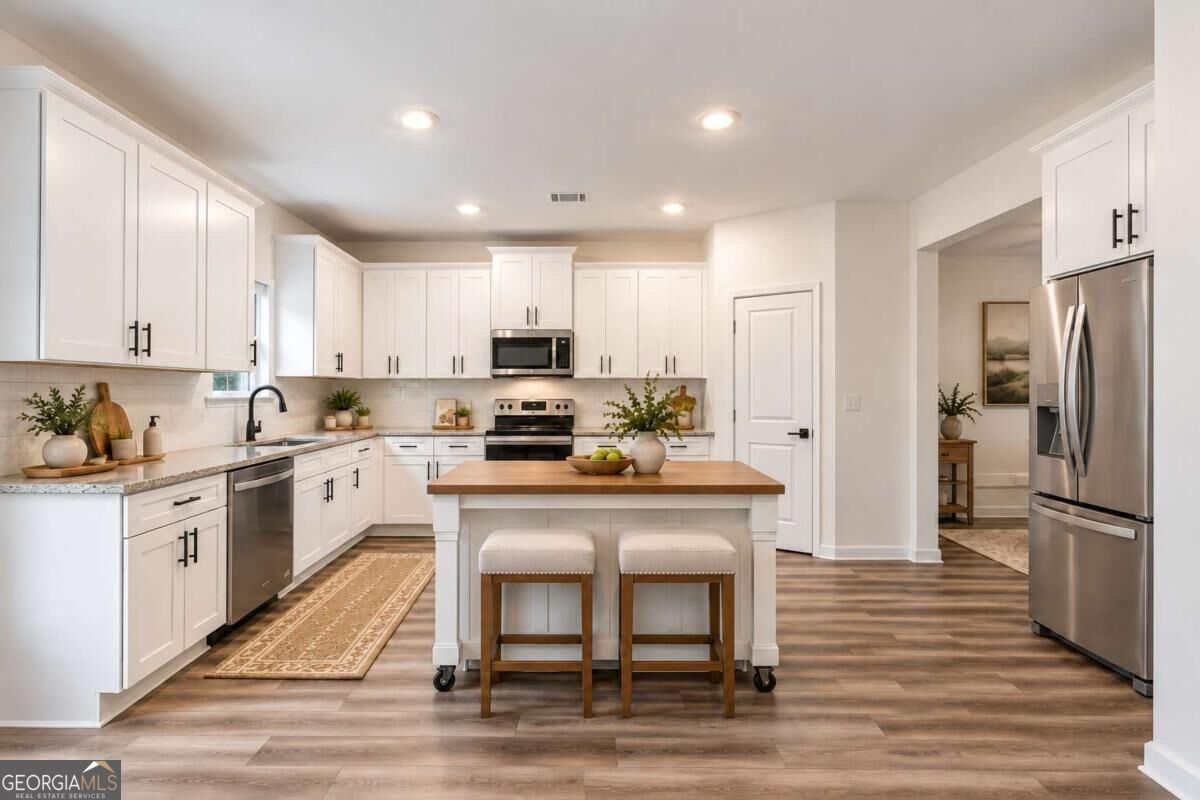 Bright white kitchen with a wood-topped island, two stools, and stainless steel appliances.