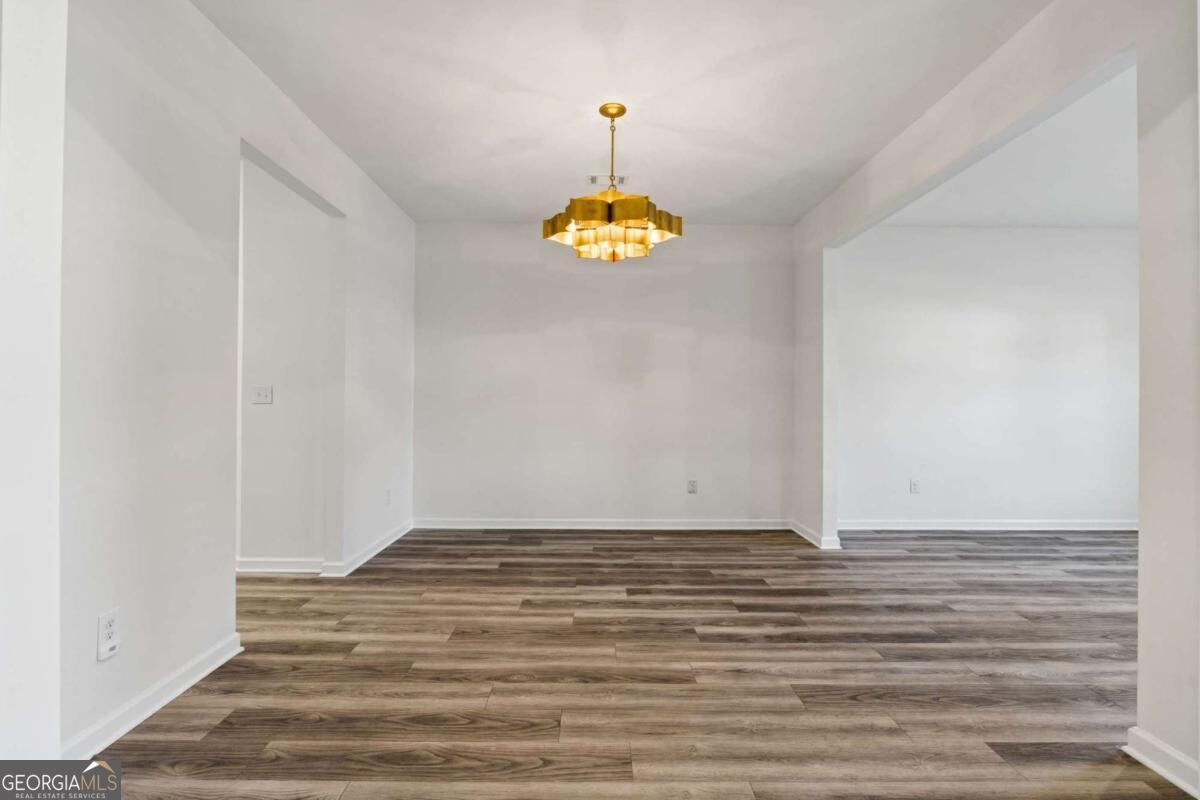Empty open room with brown plank flooring and a gold chandelier.