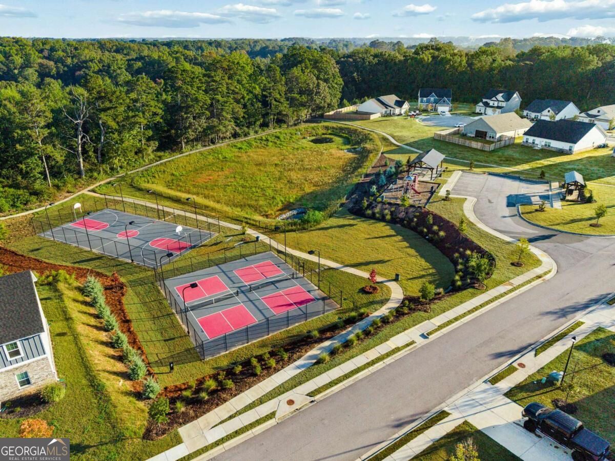 Aerial view of a residential community with fenced basketball courts and walking paths beside wooded land.