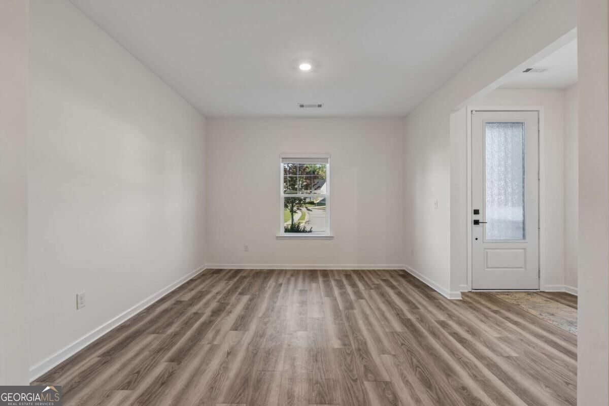Empty room with plank flooring, a rear window, and a glass-panel door.