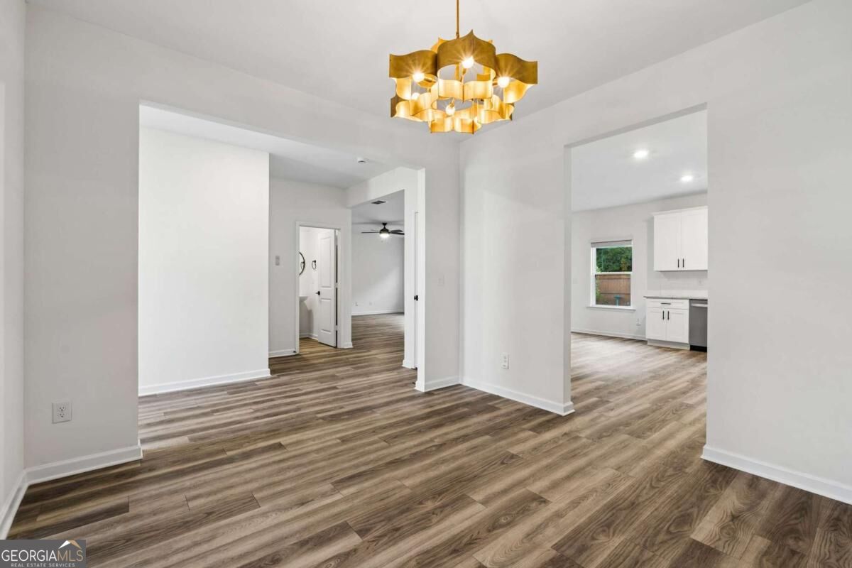 Open unfurnished interior with wood-look flooring, a gold chandelier, and a view into the kitchen.