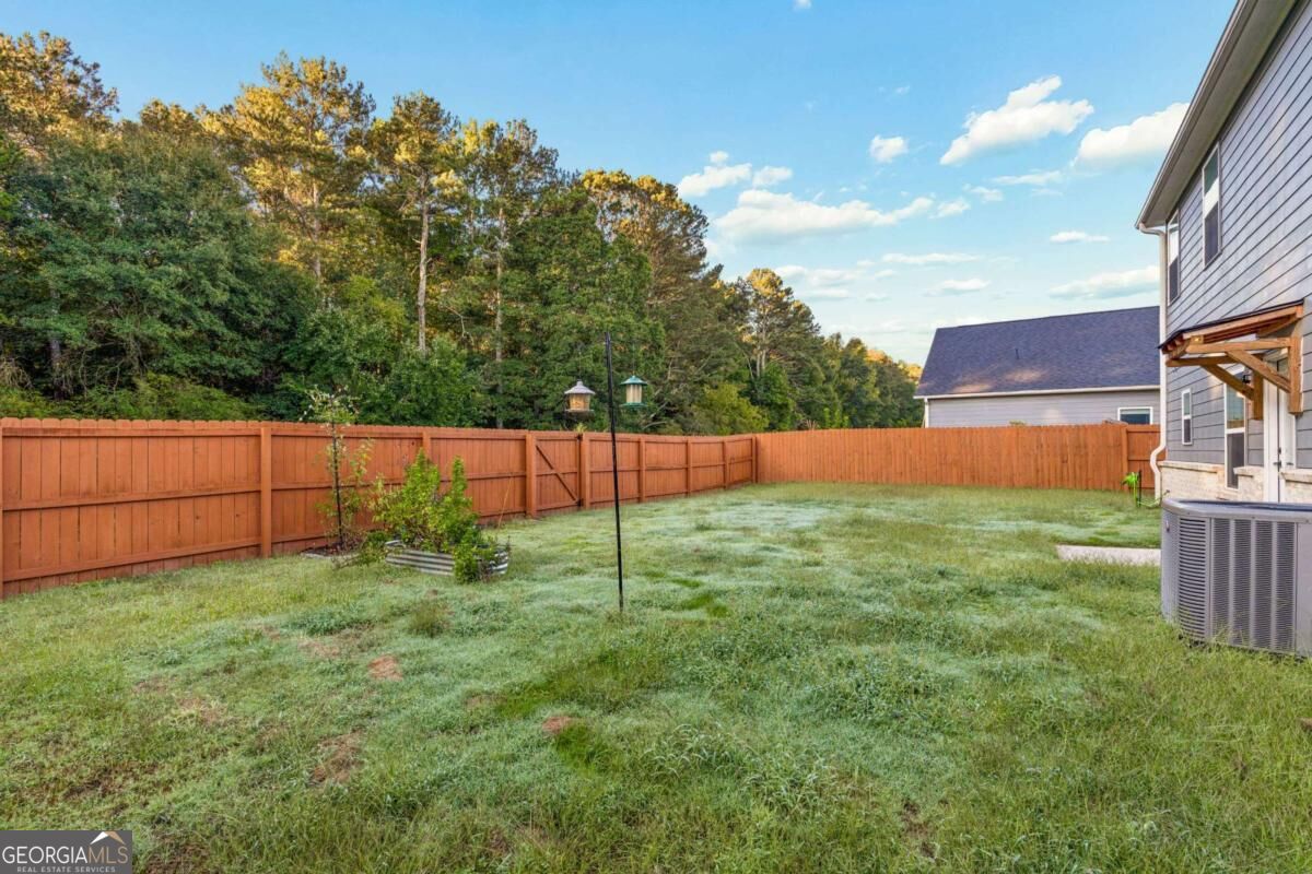 Fenced backyard with a grassy lawn, wooded tree line, and the side of the house.