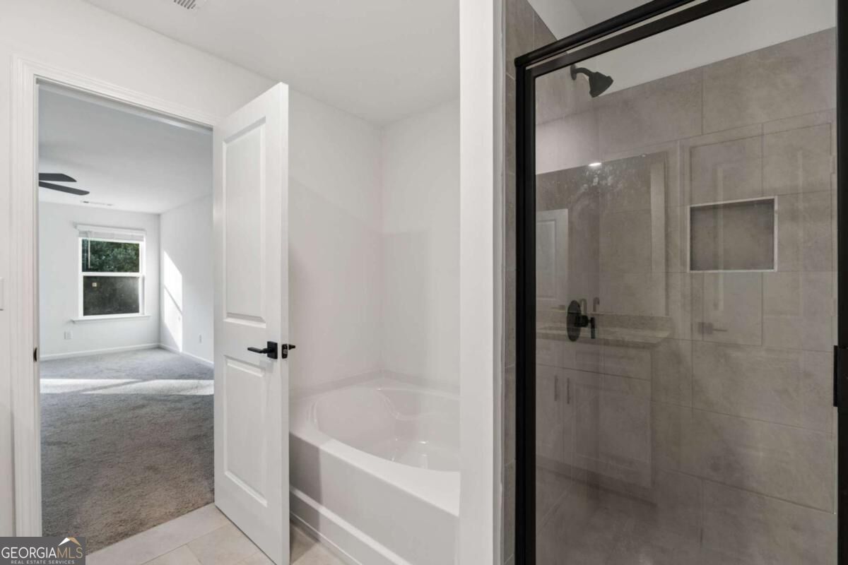 Bathroom with a white bathtub and spacious gray-tiled walk-in shower with black-framed glass.