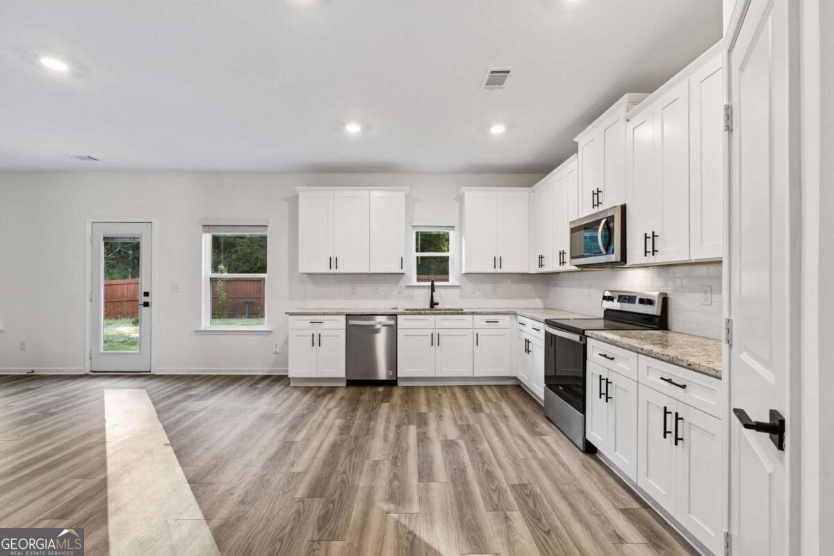 Vacant kitchen with white cabinets, stainless steel appliances, and gray-brown plank flooring.