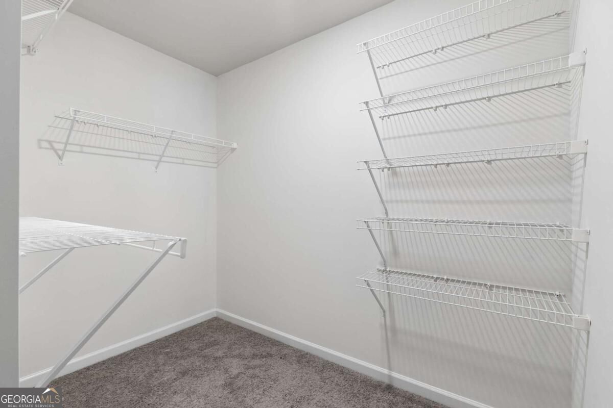 Walk-in closet with white wire shelves on three walls and gray carpet.