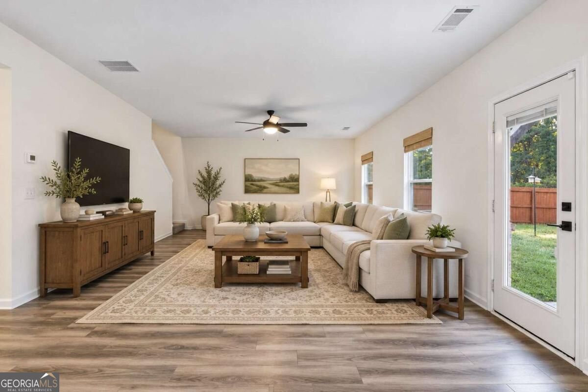 Staged living room with a cream sectional, wood furniture, and a glass door opening to a fenced yard.