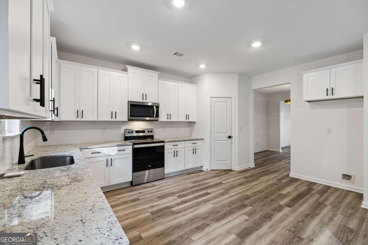 Vacant kitchen with white cabinets, granite counters, stainless steel appliances, and wood-look flooring.