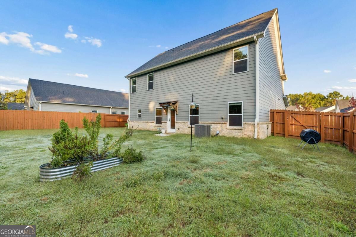 Two-story gray house viewed from its fenced backyard, with a raised garden bed and brick foundation.