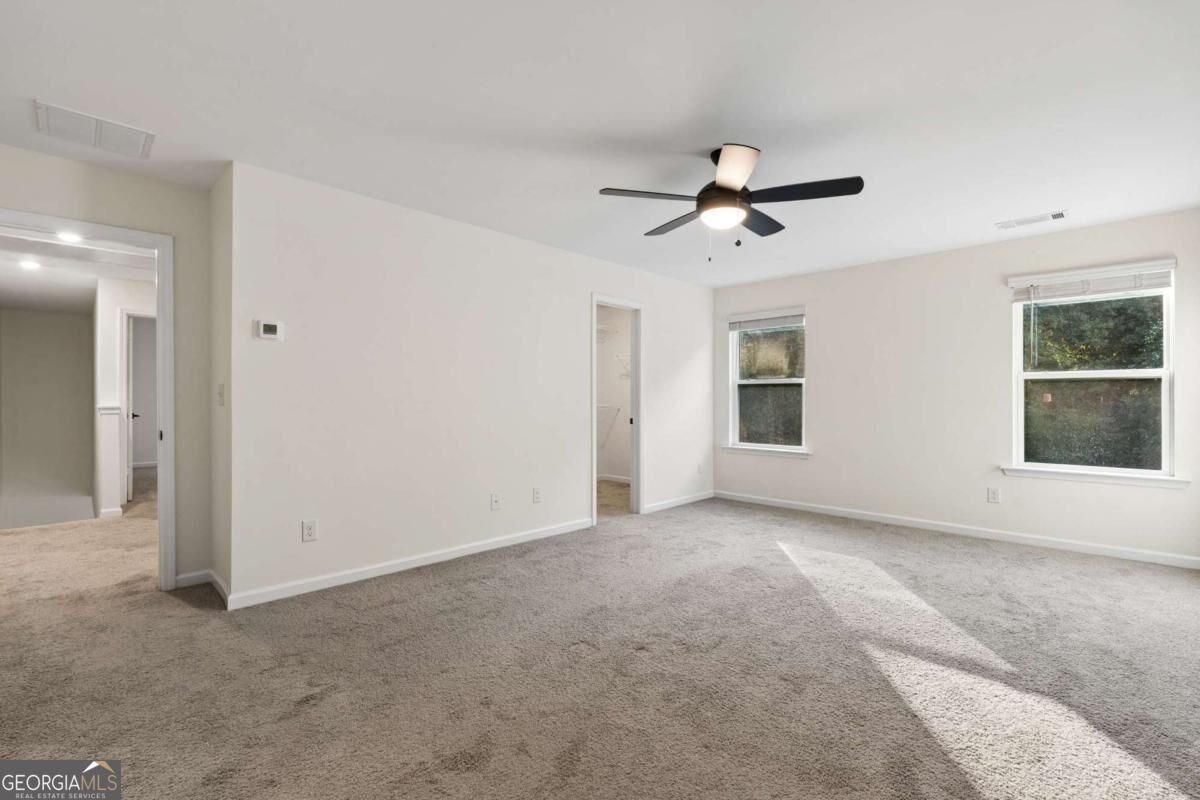 Empty carpeted bedroom with two windows and a ceiling fan.