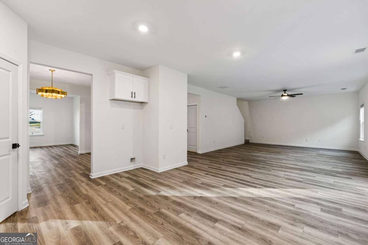 Vacant open-plan living area with brown wood-look flooring and an adjoining room with a gold chandelier.