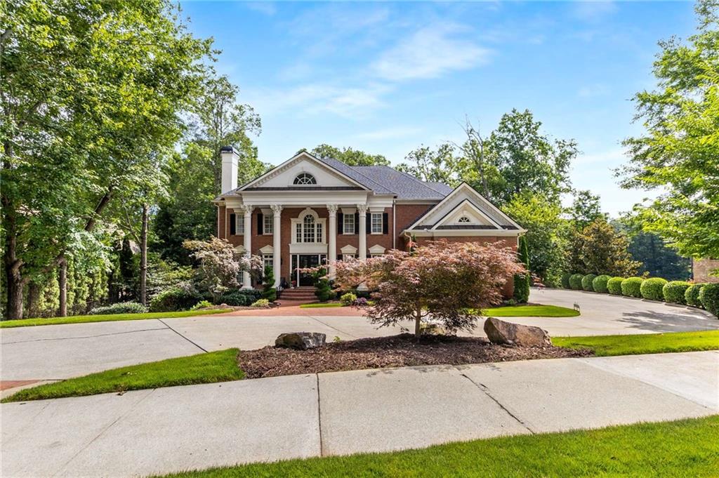 Two-story brick home with white columns, landscaped grounds, and a broad curved driveway.