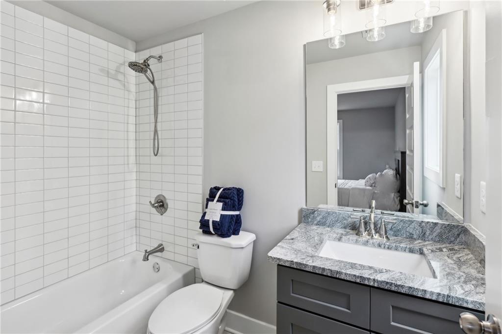 Bathroom with a white tiled tub and shower beside a dark vanity with a stone countertop.