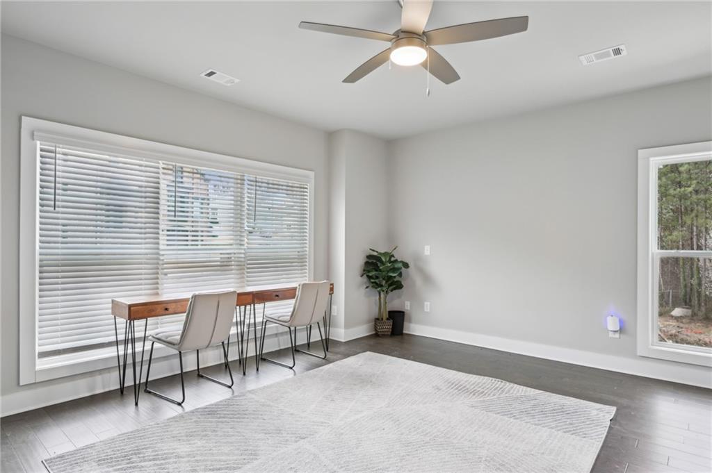 Bright room with a desk, two chairs, wide window with blinds, and ceiling fan.