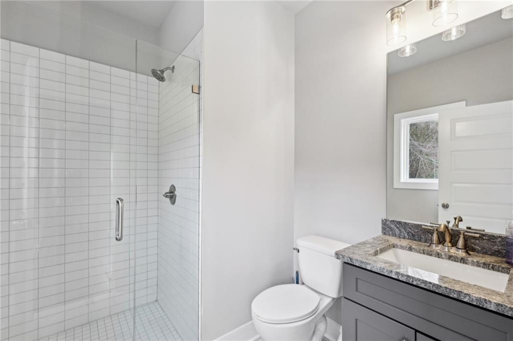 Bathroom with a glass-enclosed white tile shower and gray vanity with granite countertop.