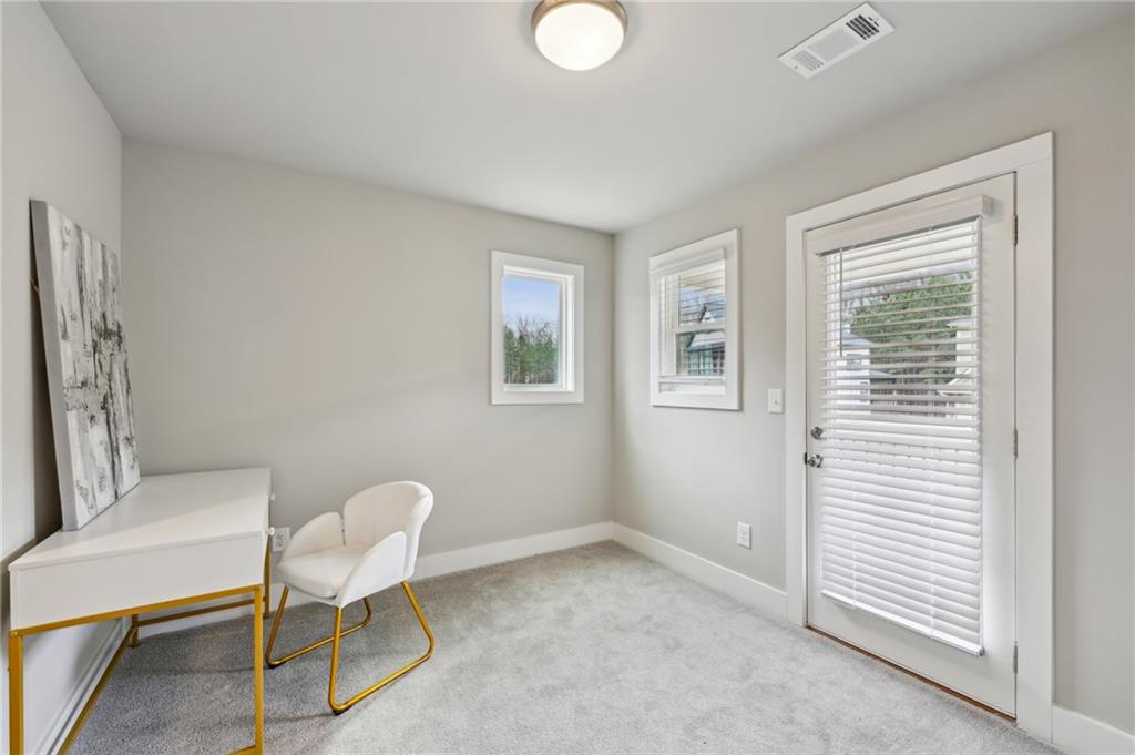 Carpeted home office with a white desk, two gold-legged chairs, and a glass door with blinds.