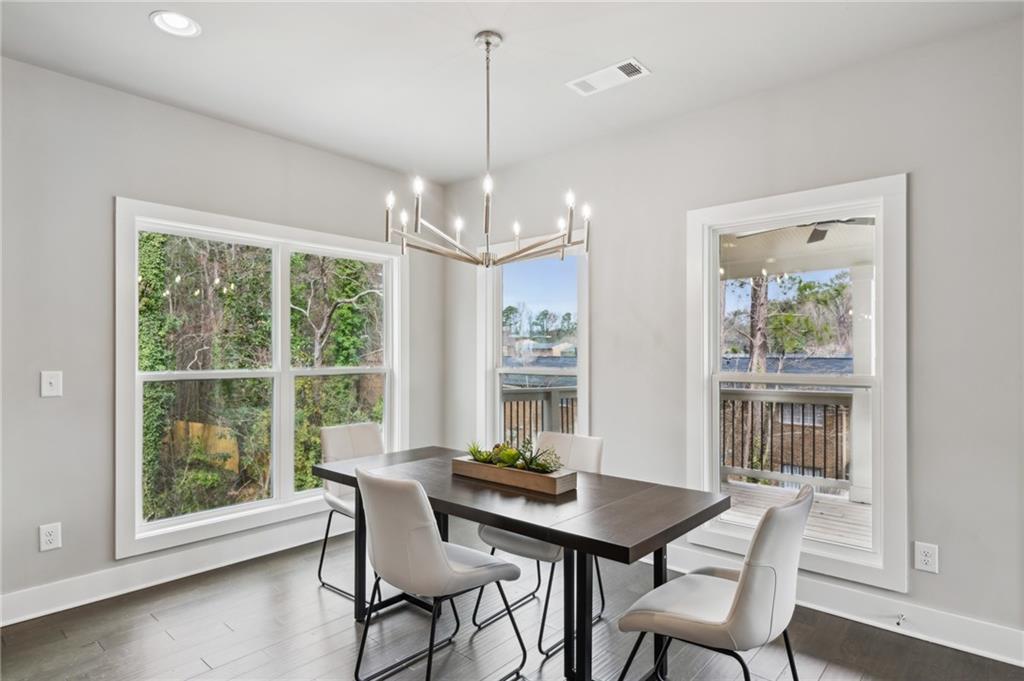 Dining room with a dark table, white chairs, modern chandelier, and large windows overlooking trees.