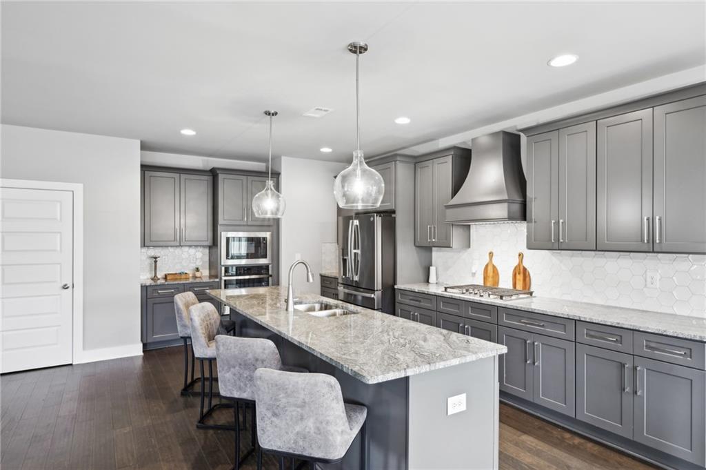 Kitchen with gray cabinets, stainless steel appliances, and a large stone island with seating.